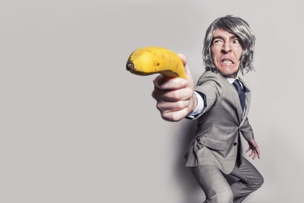 Homme en costume braquant une banane comme un pistolet